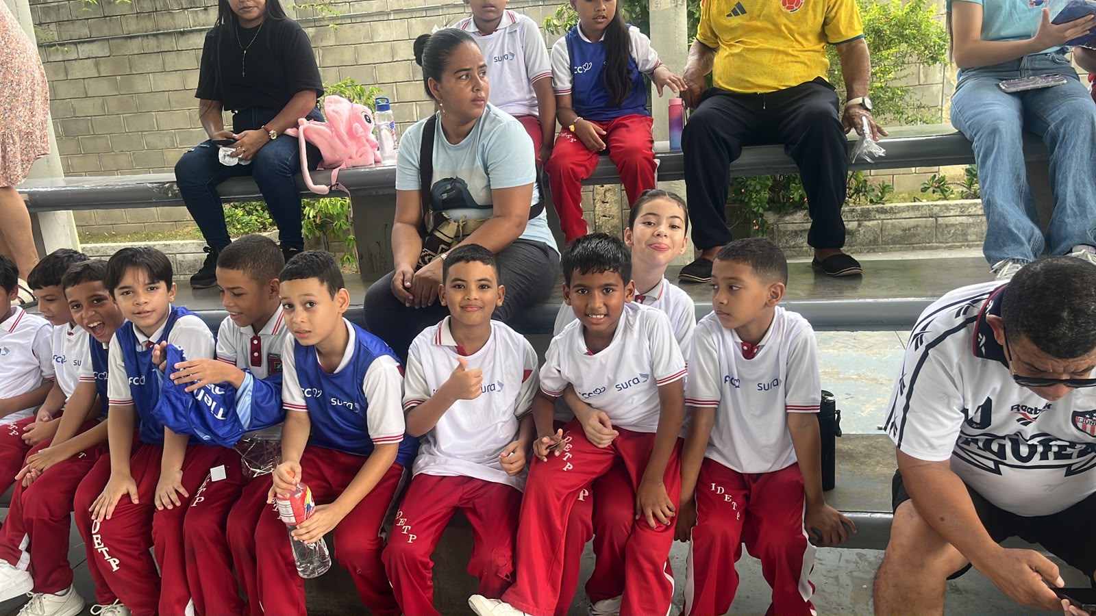 Estudiantes sentados en la gradería acompañados por sus padres